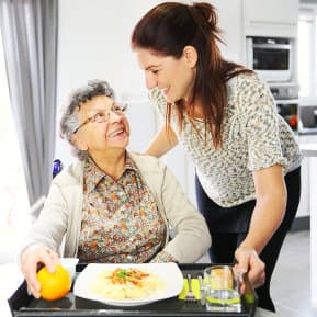 caregiver serving meal for senior woman